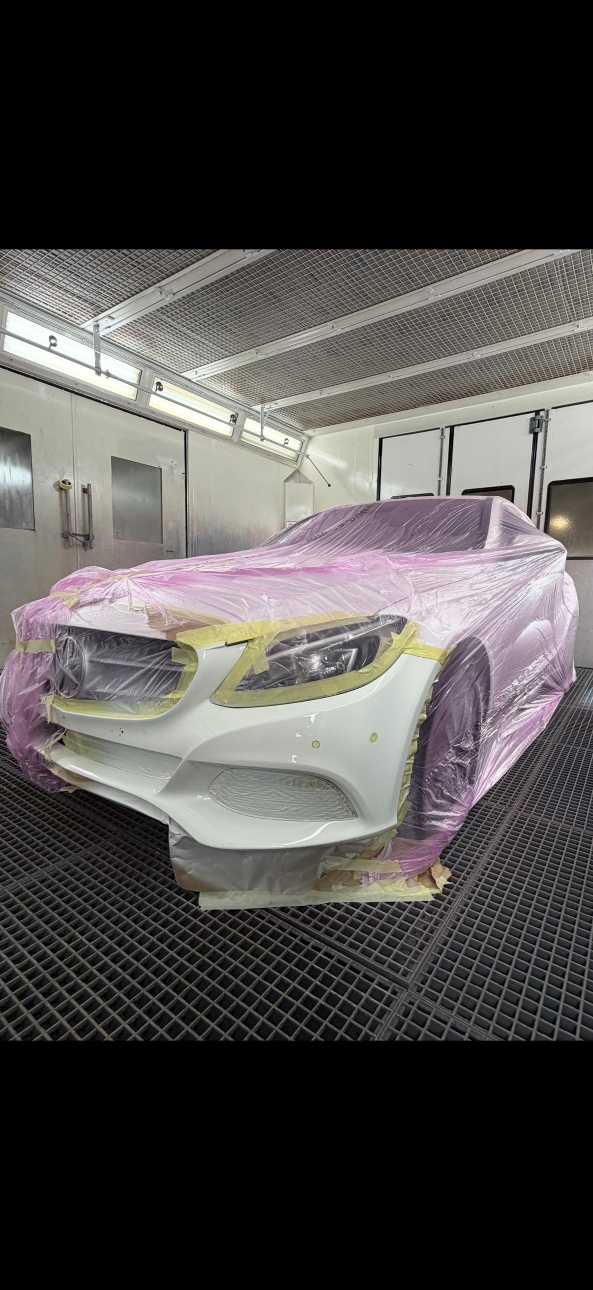 De witte voorbumper van een afgeplakte Mercedes in de spuitcabine