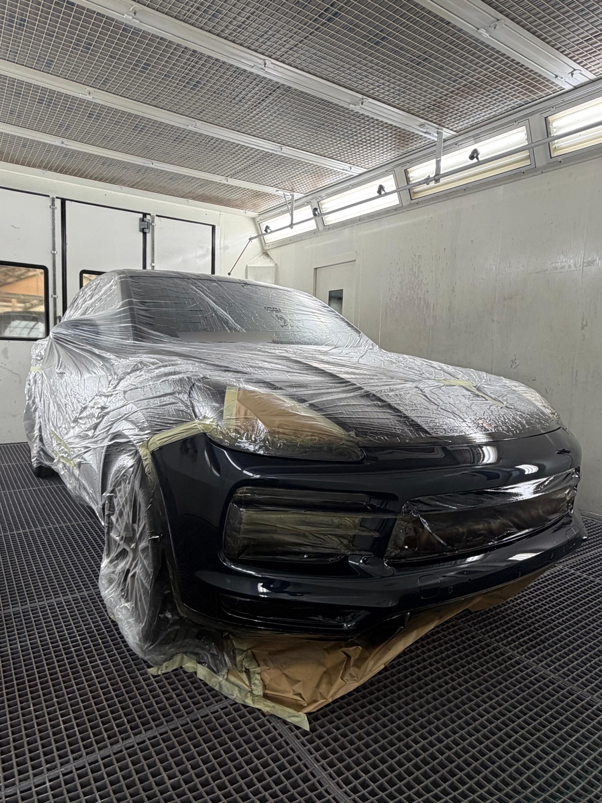 De pas gespoten voorbumper van de Porsche tijdens het drogen in de cabine, met de afplakfolie nog aanwezig