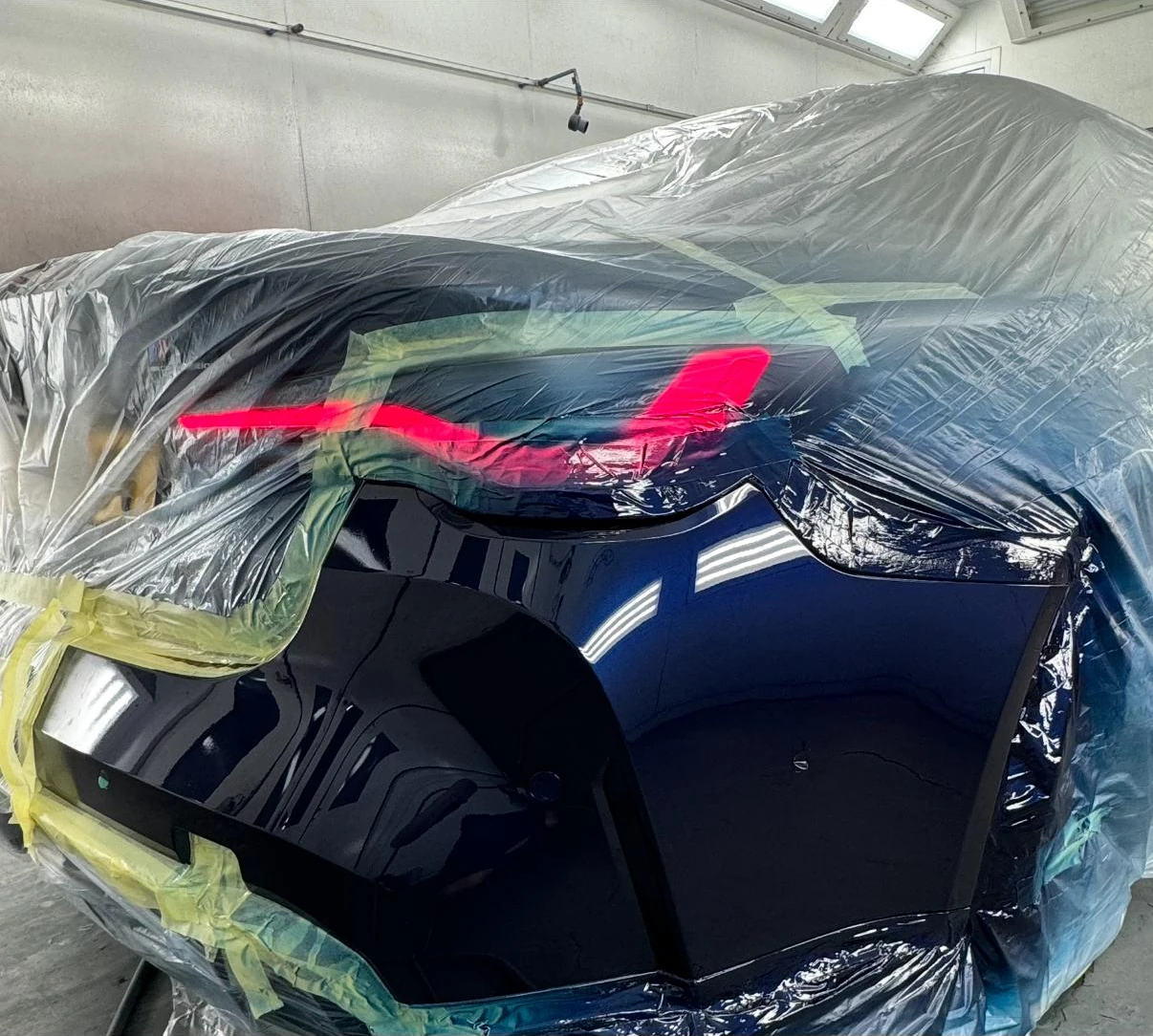 Glanzend blauw lakwerk aan de achterbumper, met de rest van de auto zorgvuldig afgeplakt